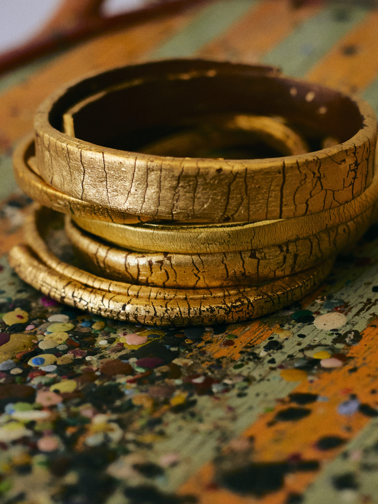 Bracciali GFW d'oro impilati sul tavolo da lavoro dipinto di Grazia